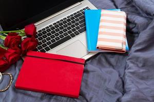 Background of laptop keyboard, empty blue and red notepads, red bouquet of flowers on the bed copy space background photo