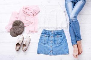 Casual summer outfit with different accessories and female legs in jeans on white wooden floor. Top view and copy space. photo