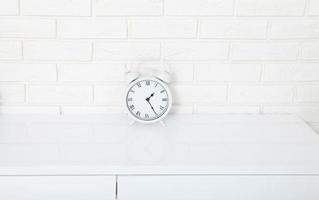 Retro alarm clock with twenty five minutes past one o'clock near brick wall on white workplace. Selective focus photo