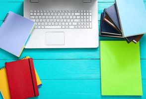 Workplace with books, keyboard, paper and other accessories on blue wooden background. Top view and copy space photo