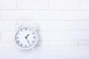 White retro alarm clock near brick wall on white workplace. Selective focus and copy space photo