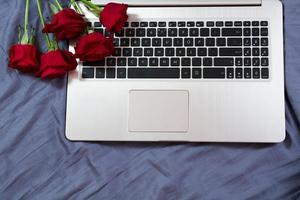 Laptop keyboard and red flowers background on bed close up. Working place concept photo