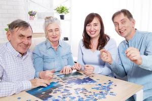 felices padres ancianos y pareja de mediana edad trabajando juntos en un rompecabezas en casa foto