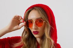 Closeup woman face in red sunglasses isolated on white background. Girl in red hoodie sweatshirt and red lips makeup. Fashion Beauty concept. Beautiful face skin and fashionable accessories concept. photo