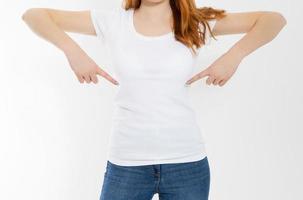 T-shirt design and advertising concept. Style and fashion. Indoor shot of cheerful smiling youngred head woman with red hair pointing index finger at copy space on her blank white top. photo