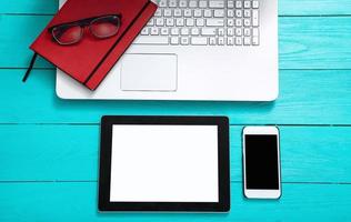 Electronic devices with copy space and keyboard on blue wooden background. Glasses and working accessories. Top view photo