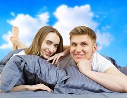 Happy beautiful couple in bed isolated on blue sky background, stay at home concept, coronavirus quarantine background, self isolation, life style at home photo