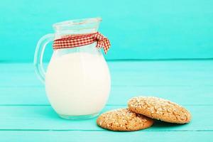 Jug of milk with plaid ribbon and oat cookies on blue wooden kitchen. Copy space, selective focus photo