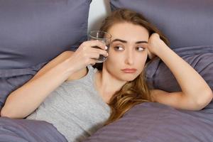 Feeling bad from a hangover in the morning  young woman hold glass of water and lying in bed bedroom photo