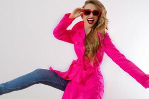 Close up happy girl in red sunglasses and pink coat isolated on white background. excited, shock and surprised young woman, trendy outfit. Fashion and shopping concept. Long wavy hair. Selective focus photo