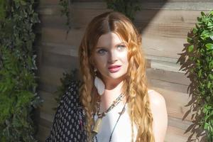 A beautiful girl with red curly hair stands at the wooden wall around the plan in the sunlight. photo