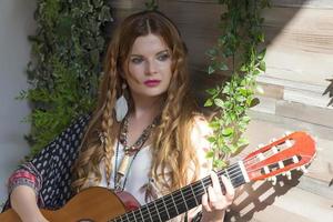 A beautiful girl with red curly hair stands and holds a seven-string guitar in her hands. photo