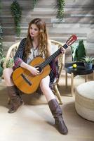 A beautiful girl with red curly hair sits on a chair with a seven-string guitar. photo