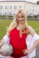 rubia con una pelota en el campo de fútbol con uniforme rojo. foto