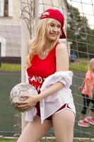 la rubia en forma roja con una pelota en la puerta del campo de fútbol. foto