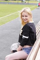 The girl sits on the bench at the football field with the ball. photo