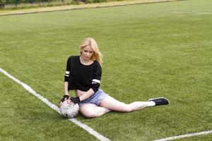 la niña está sentada en el campo de fútbol con la pelota. foto