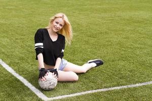 The girl is sitting on the football field with the ball. photo