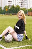 The girl is sitting on the football field with the ball. photo