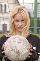 hermosa rubia con una pelota en la portería de fútbol. foto