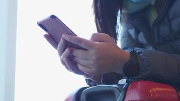 gros plan des mains d'une femme asiatique portant un masque assise et utilisant un smartphone, tapant sur son smartphone pour envoyer des messages à ses amis. attendant le vol à l'aéroport avec sa valise video