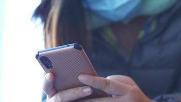 Close up hands of Asian woman wearing mask sitting and using smartphone, typing on her smartphone to send her friend messages. Close up using phone concept video