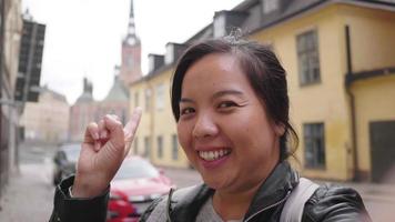 Happy Asian woman recording video her self on smartphone in Sweden, going out for a walk on the street in Sweden. Traveling abroad on long holiday. beautiful building background