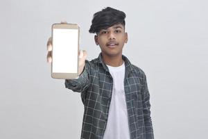 estudiante universitario indio que muestra la pantalla móvil sobre fondo blanco. foto