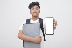 Young indian student holding file and showing smartphone screen on white background. photo