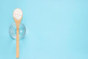 Fish collagen peptides powder and glass of water on blue background. photo