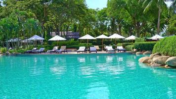 hermosa sombrilla y silla de lujo alrededor de la piscina al aire libre con palmeras de coco en el cielo del atardecer o del amanecer - concepto de vacaciones y vacaciones video