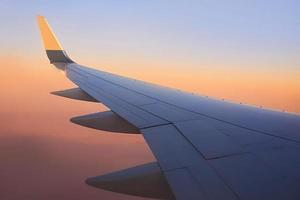 vista al ala del avión en el cielo durante la puesta de sol. concepto de viaje y transporte foto