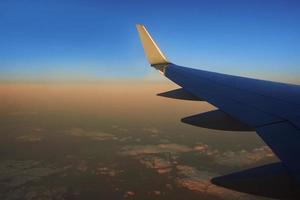 vista al ala del avión en el cielo durante la puesta de sol. concepto de viaje y transporte foto