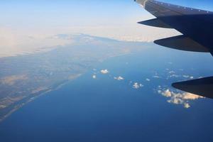 View to the wing of airplane in the sky and the sea. Travel and transportation concept photo