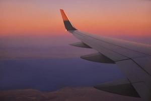 vista al ala del avión en el cielo durante la puesta de sol. concepto de viaje y transporte