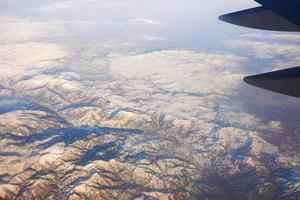 View to the wing of airplane in the sky and snowy mountains. Travel and transportation concept photo