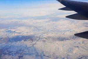 View to the wing of airplane in the sky and snowy mountains. Travel and transportation concept photo