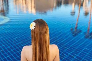 espalda de la mujer con flor sentada al borde de la piscina.
