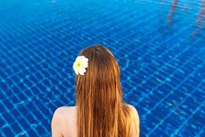 back of the woman with flower sitting on the edge of the swimming pool.