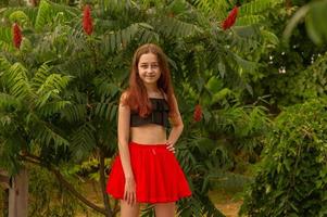 Teenage girl in a black top and red skirt on a summer wood background. Holidays. Girl 10 years old. photo