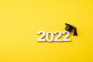 Graduat hat with wooden number 2022 on yellow background. Education, leaning, class 2022 concept photo