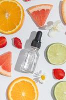 Top view of vitamin C dropper, serum, cosmetic oil and slices of orange, lime, grapefruit on white background photo