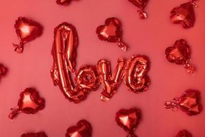 Festive background for Valentine's Day from Foil balloons shape heart and love word on red background photo