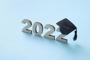 Graduation 2022 wearing graduate hat on wooden number 2022 on blue background. Variative focus photo