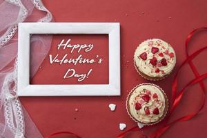 Two cupcakes with cream and decor, angel, frame on a red background. photo