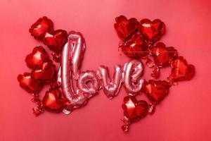 piso festivo para el día de san valentín de globos de aluminio en forma de corazón y palabra de amor sobre fondo rojo foto