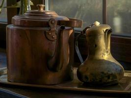 Two copper kettles for tea on a windowsill illuminated by sunlight at sunset. Contrast of light and shadow photo