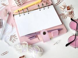 el diario se abre con una página blanca y holográfica. planificador rosa con lindos artículos de papelería fotografiando en estilo flatlay. vista superior del planificador rosa con papelería comercial foto