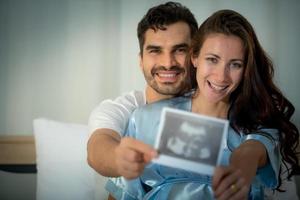 la felicidad de una mujer embarazada y su esposo en el dormitorio con la película de ultrasonido foto