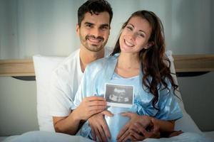 The happiness of a pregnant woman and her husband in the bedroom with the ultrasound film